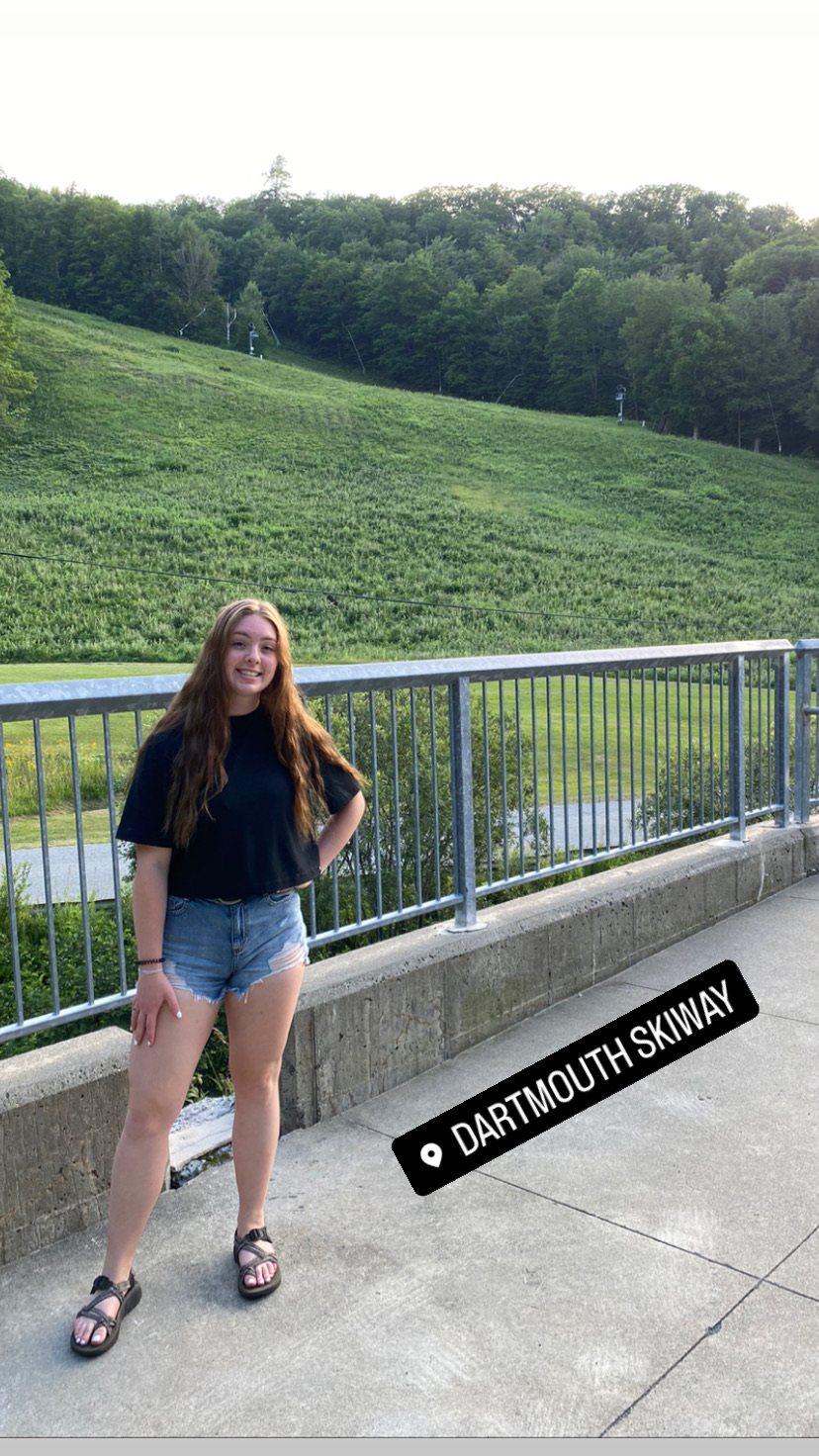  Picture of Tayler Huntley standing in front of grassy mountains. The picture also includes a lacation tag that says 